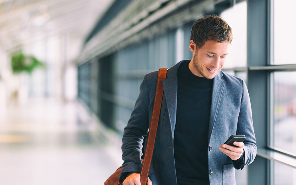 photo of young casually dressed businessman looking at his cellphone walking through airport